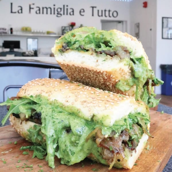 Two halves of a large sub sandwich with green sauce, meat, and arugula, at La Famiglia e Tutto.