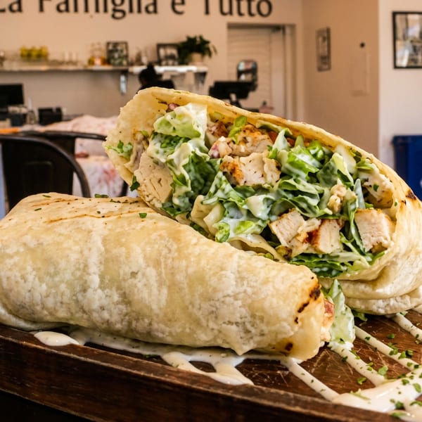 Chicken Caesar wrap cut in half on a wooden board with sauce, in a restaurant setting.