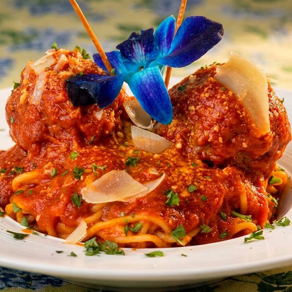 Spaghetti and meatballs in red sauce, garnished with Parmesan and a blue orchid.