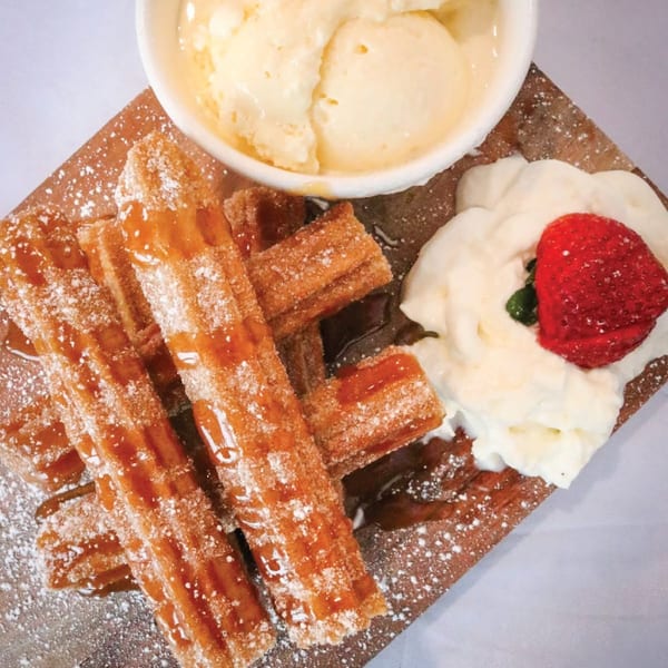 Churros drizzled with caramel, powdered sugar, served with vanilla ice cream, whipped cream, and a strawberry.